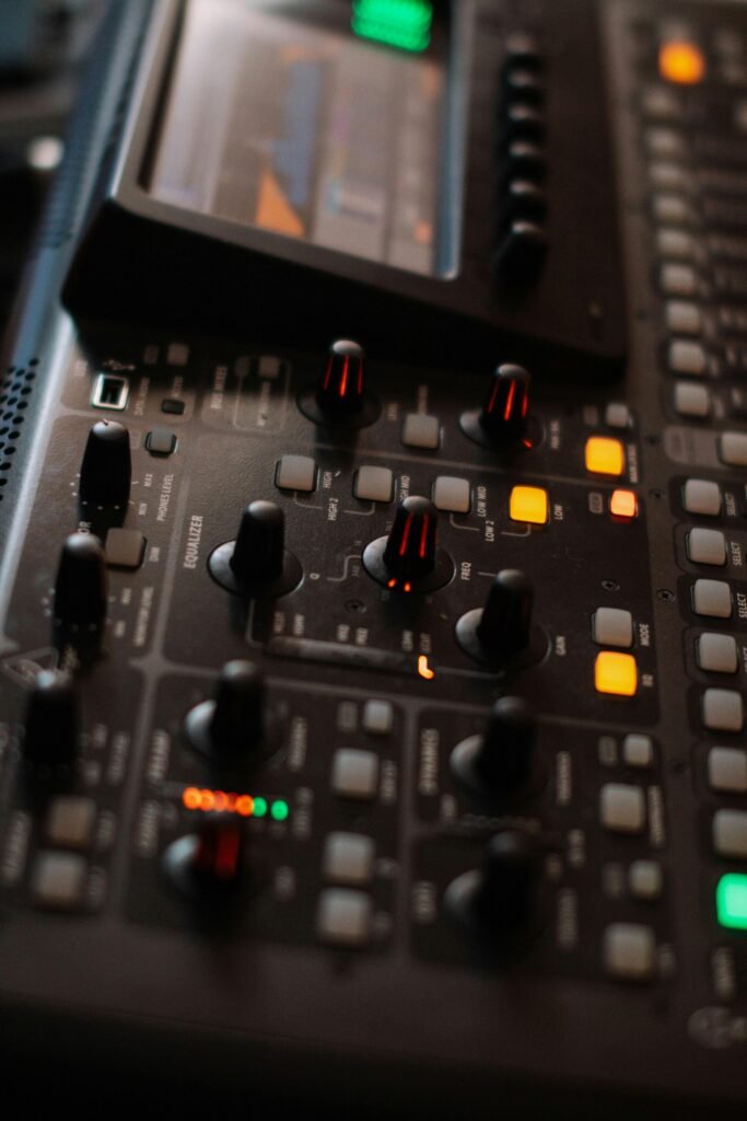 pexels-photo-12889651-12889651 Detailed view of audio mixing console with illuminated controls and digital screen.